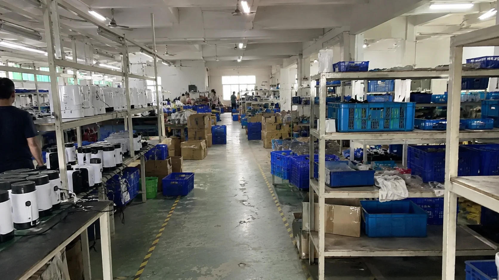 Pasillo de fábrica con bancos de montaje, estantes, piezas y cartones preparados
